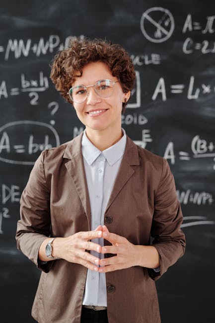 Teacher standing by a blackboard with algebra equations, smiling confidently.